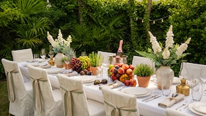 Mobiliario de comedor exterior con una mesa dispuesta para seis personas, rodeado de abundante vegetación.