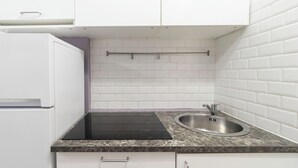 A compact kitchen with white cabinets, a black induction cooktop, and a stainless steel sink. - Italianway - Orti 5 (Milan)