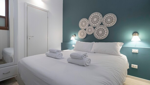 A neatly made bed with white linens and towels, a teal accent wall with decorative wall art, and bedside lamps. - Italianway - Orti 5 (Milan)