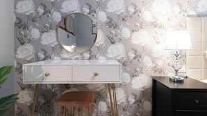 A vanity with a round mirror, a stool, and a lamp on a dresser against floral wallpaper. - Italianway - Orti 5 (Milan)