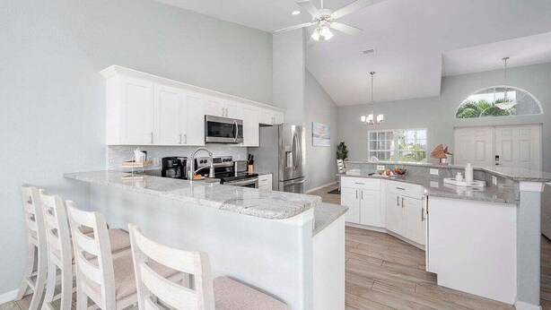A modern kitchen with white cabinetry, a large island, and a ceiling fan.