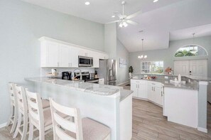 A modern kitchen with white cabinetry, a large island, and a ceiling fan. - Wave N Sea - Waterfront Home with Outdoor Partial (Cape Coral)