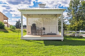 A gazebo with a covered seating area, a fan, and a grill.