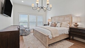 A bedroom with a wooden bed, a chandelier, a TV mounted on the wall, and a window with blinds. - Dixieland Delight at River Rocks Plantation (Guntersville)