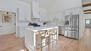 A modern kitchen with white cabinetry, a stainless steel refrigerator, and a central island with bar stools. - Dixieland Delight at River Rocks Plantation (Guntersville)
