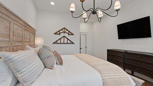 A bedroom with a bed, a chandelier, a dresser, a TV, and a door. - Dixieland Delight at River Rocks Plantation (Guntersville)