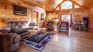 A log cabin interior with a living room, dining area, and kitchen.