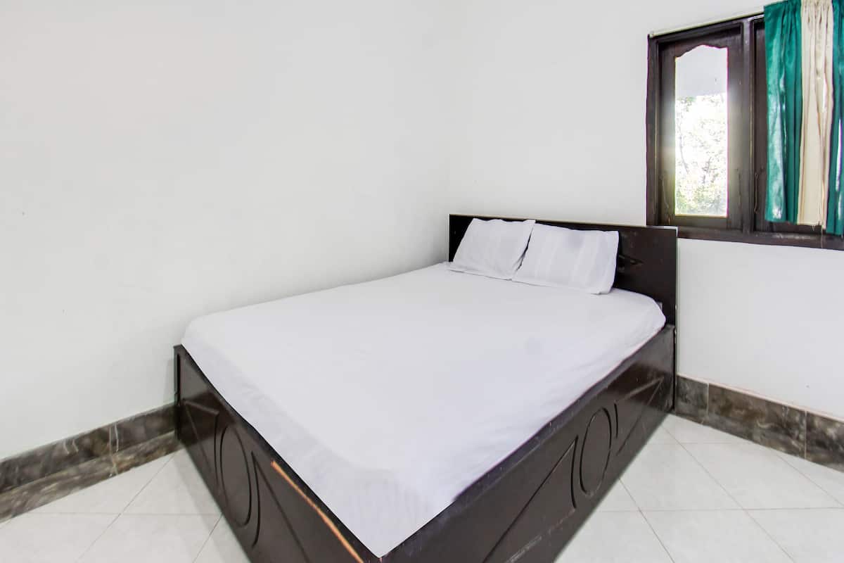 Een enkel bed met houten frame en wit beddengoed in een kamer met witte wanden en een betegelde vloer.