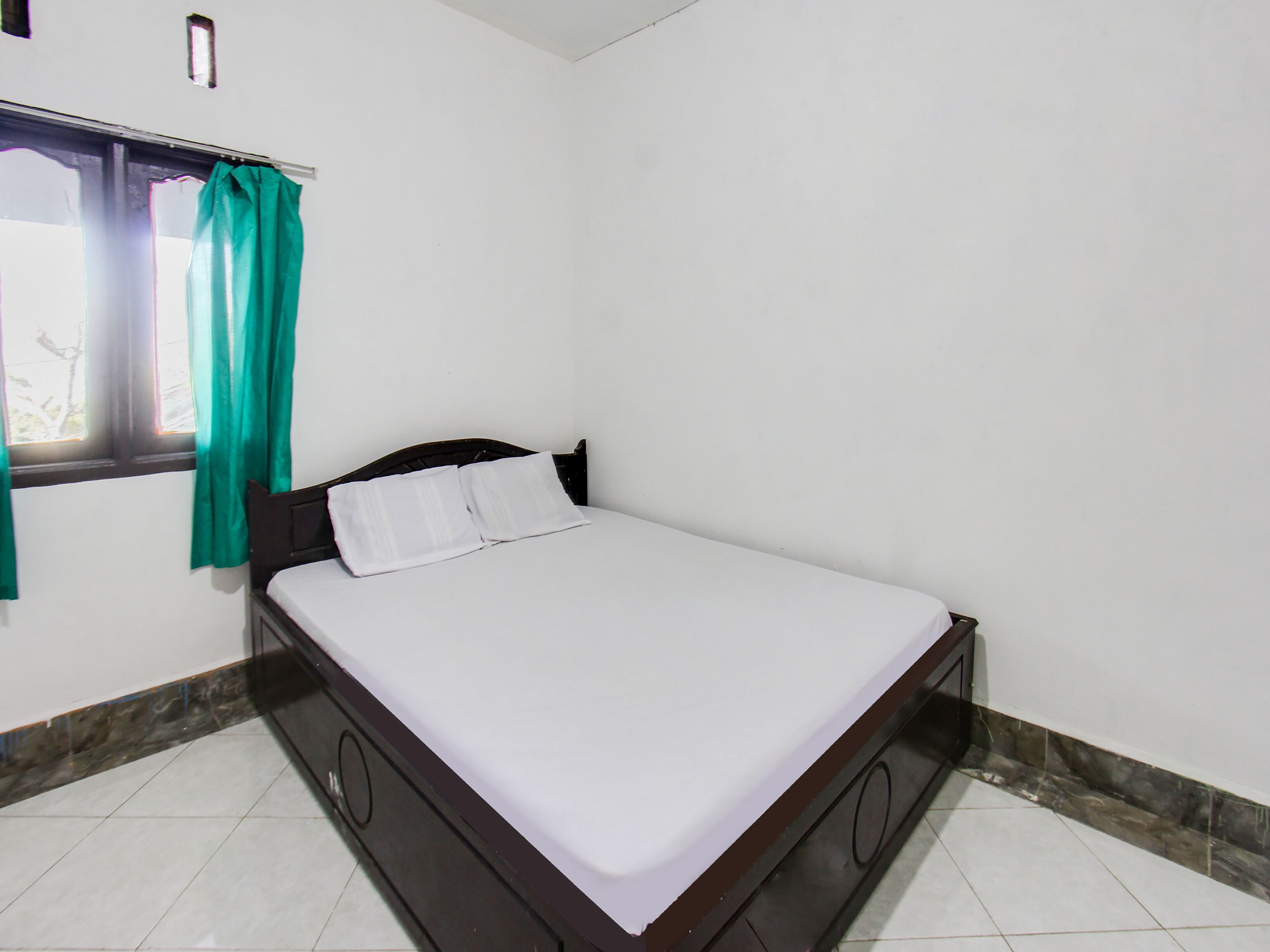 A single bed with a wooden frame and white bedding in a room with white walls and a tiled floor.