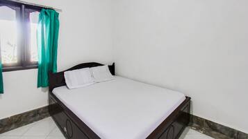 A single bed with a wooden frame and white bedding in a room with white walls and a tiled floor.