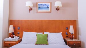 Een net opgemaakt bed met witte lakens, een groen sierkussen en twee bedlampjes.