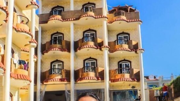 Een hotel met een zwembadgedeelte, met een meerlaags gebouw met balkons en een helderblauwe lucht.