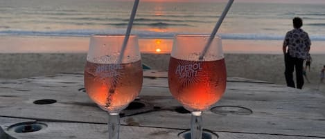 Two glasses of Aperol Spritz on a wooden table with a sunset view.