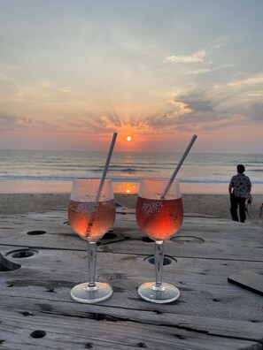 Two glasses of Aperol Spritz on a wooden table with a sunset view.