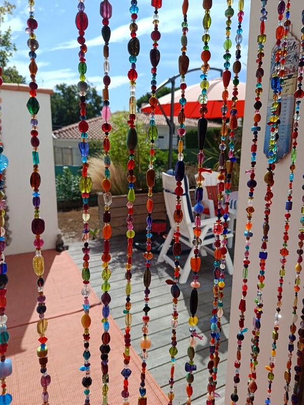 A patio area with a wooden deck, outdoor furniture, and a colorful beaded decoration hanging in the foreground.