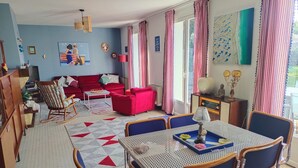 Et spiseområde med et bord og stole, en rød sofa og en gyngestol.