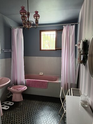 Een badkamer met een badkuip, toilet, wastafel en een raam met gordijnen.
