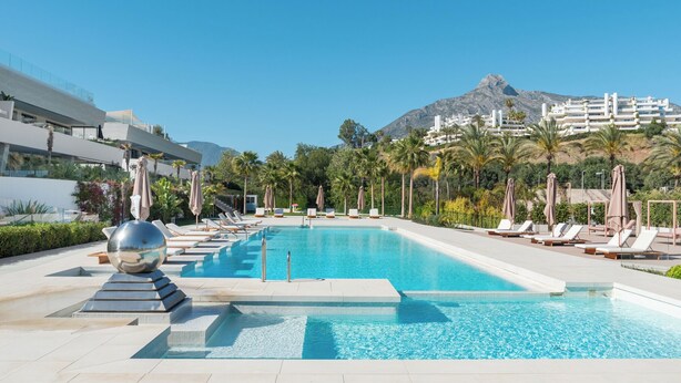 A swimming pool with lounge chairs, a modern building, and a mountain in the background. - Exceptional 3 bedroom duplex penthouse in Epic Marbella (Marbella)