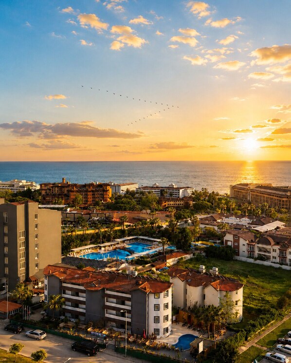 Un resort con varias edificaciones, una piscina y vista al mar al atardecer.