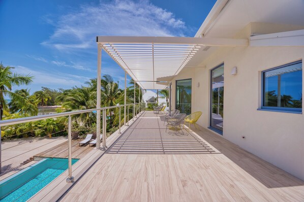 A modern outdoor balcony with a pool, lounge chairs, and a view of palm trees.