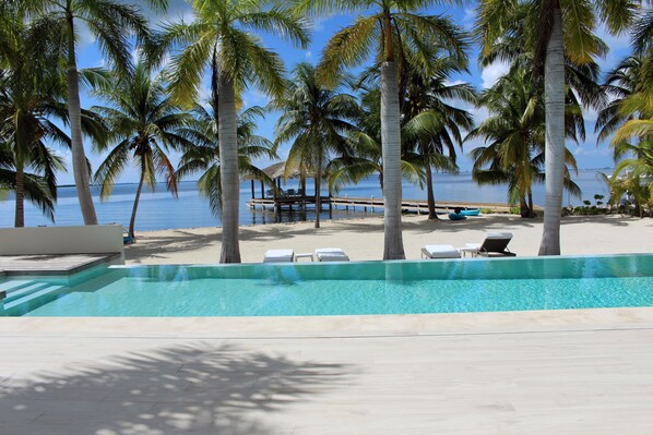 Un área junto a la piscina con sillones de descanso, un muelle de madera y palmeras.