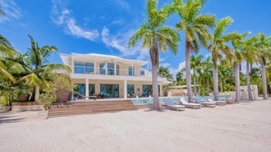 Una propietat moderna a peu de platja amb piscina, palmeres i un edifici de dos pisos.