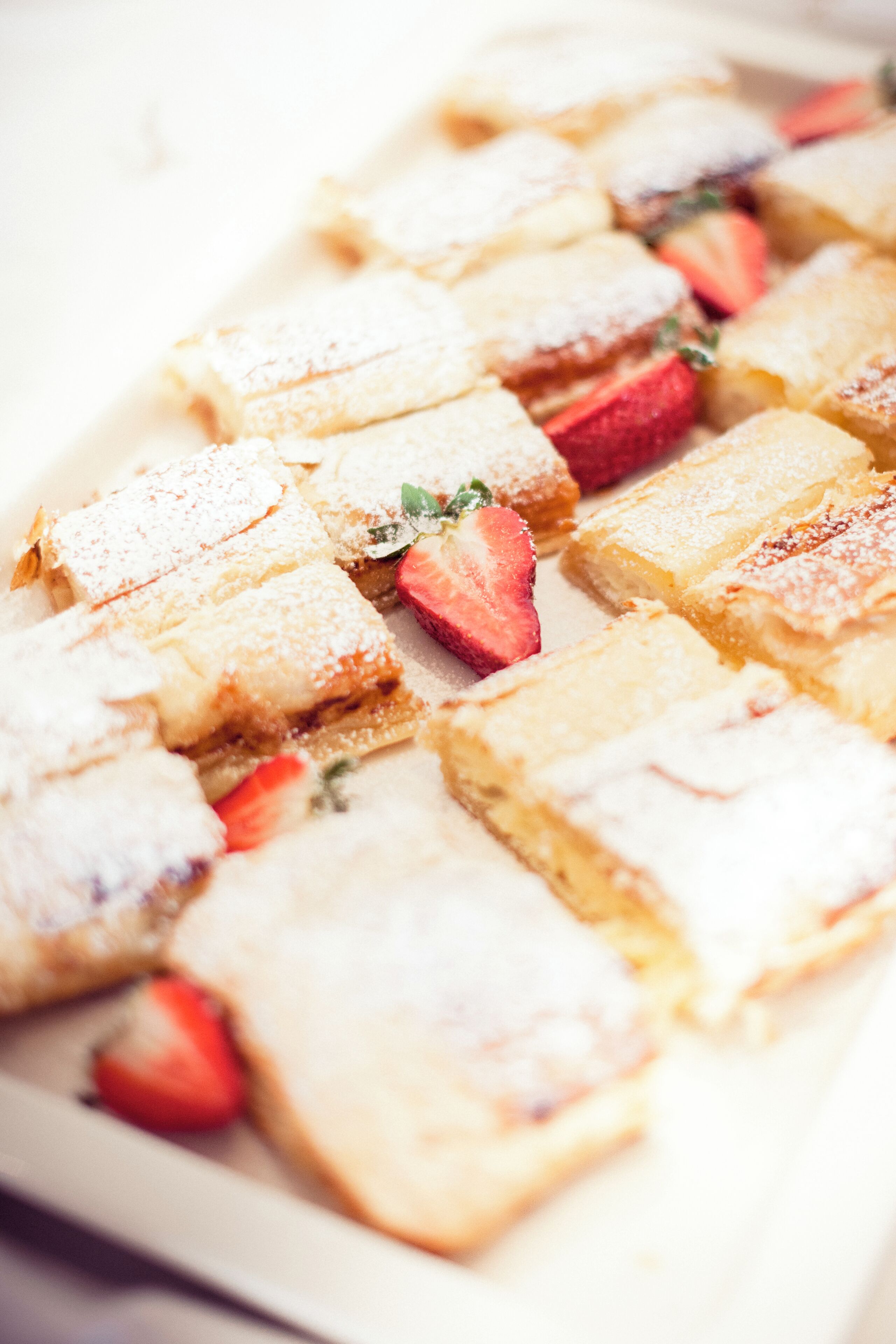 Un plat amb pastissos quadrats polvorosos i decorats amb maduixes.