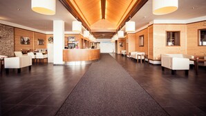 Un hall d’entrée spacieux avec un comptoir d’accueil central, des espaces de détente et des panneaux de bois sur les murs.