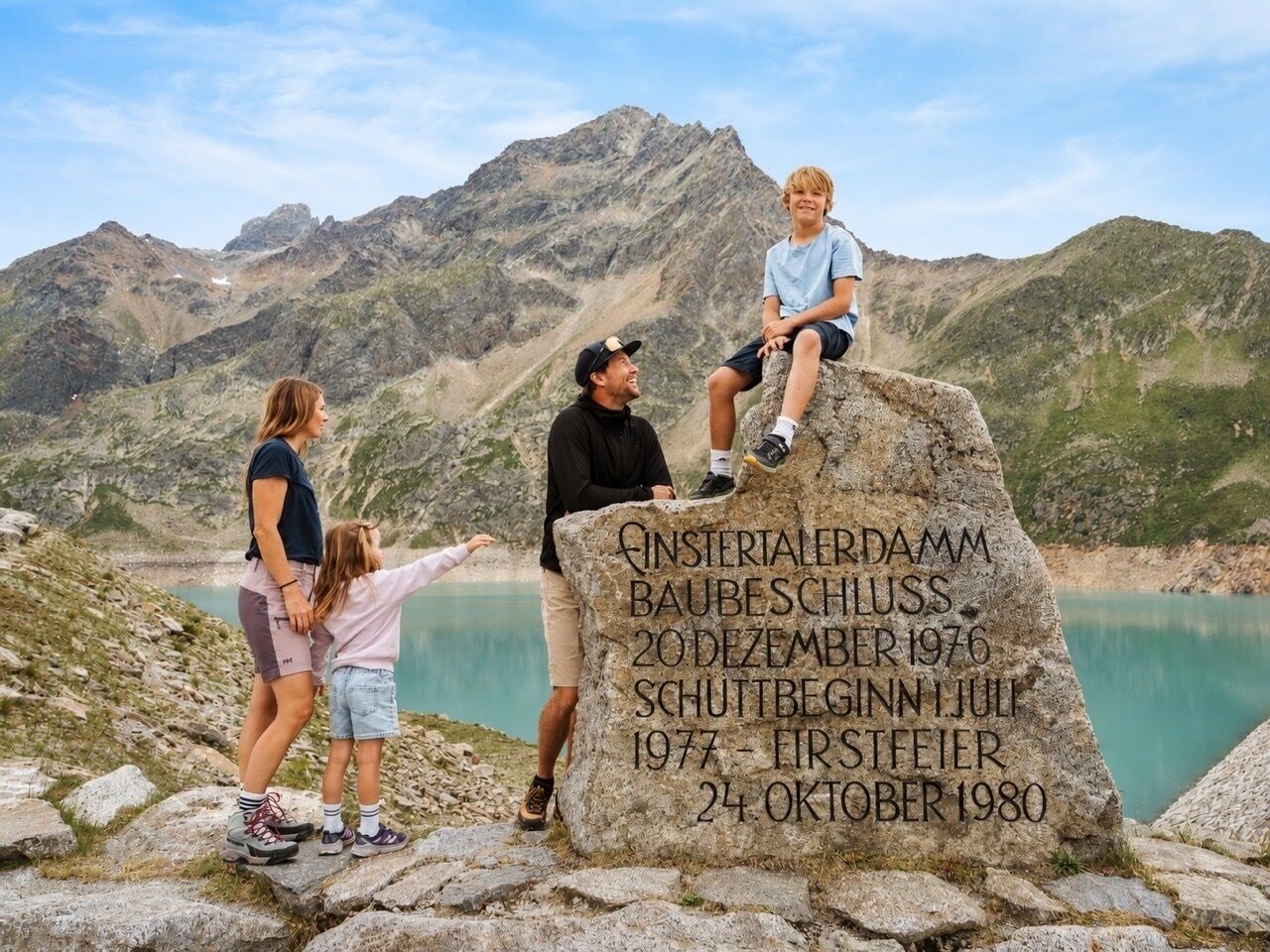 A memorial stone with inscriptions, surrounded by a mountainous landscape and a body of water.