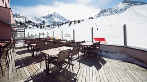 Un espace extérieur aménagé avec des tables et des chaises, offrant une vue sur un paysage montagneux enneigé et une piste de ski.