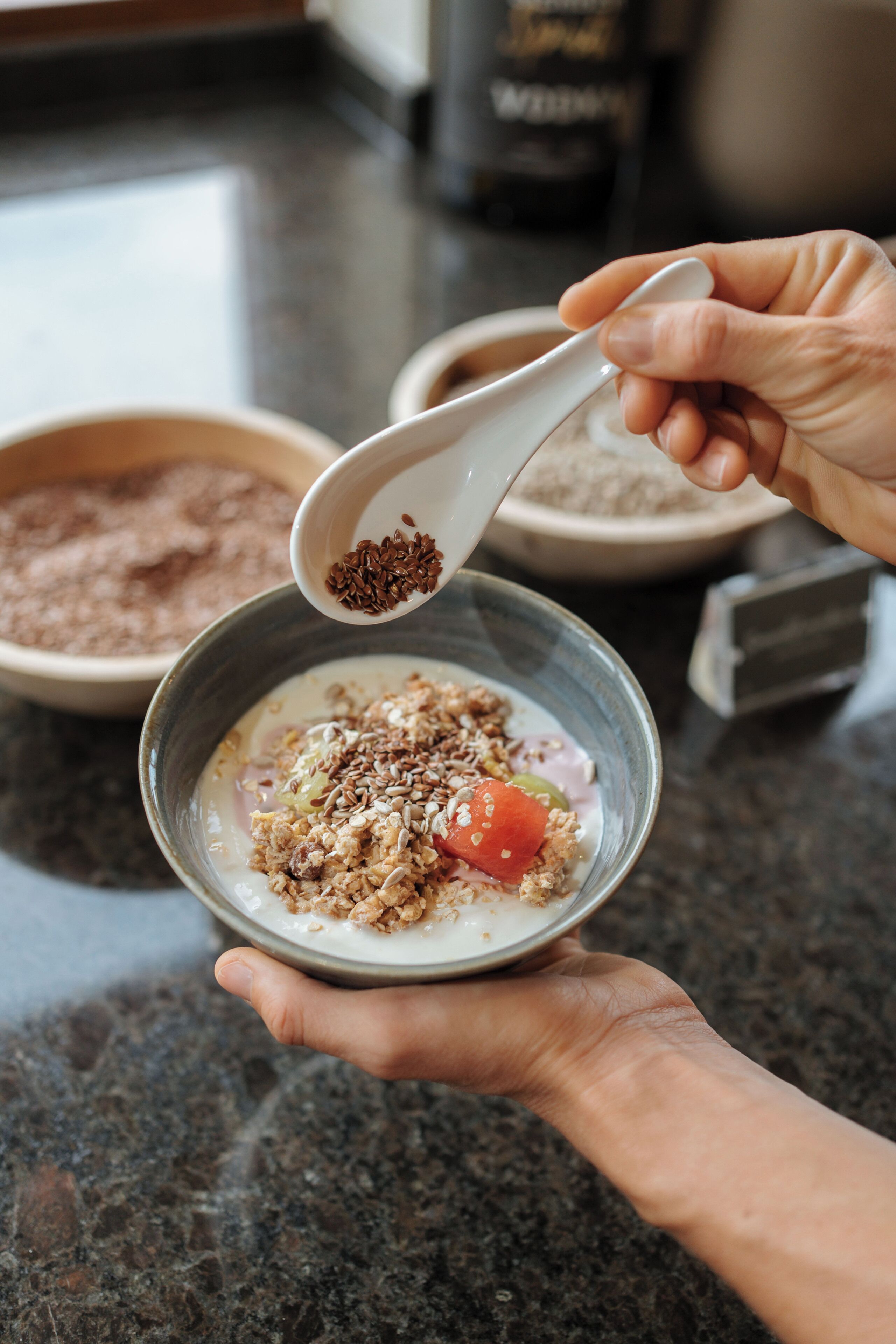 A bowl of cereal with milk and a spoonful of seeds being added.