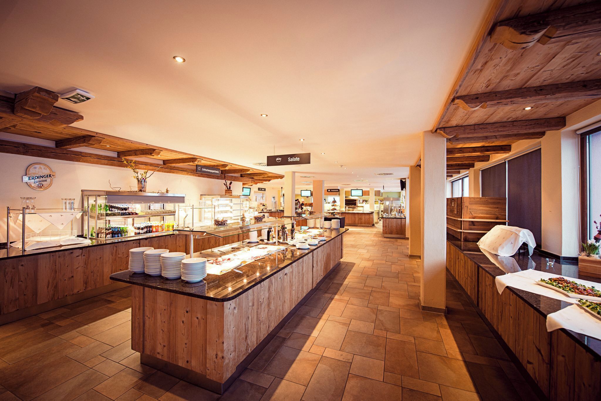 Eine moderne Hotelhalle mit Holzelementen, einem zentralen Buffetbereich und einem Schild, das den Standort des Salatsorts angibt.
