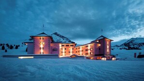 Un grand hôtel à plusieurs étages, doté d’une tour centrale et de deux tours plus petites, entouré de montagnes enneigées.
