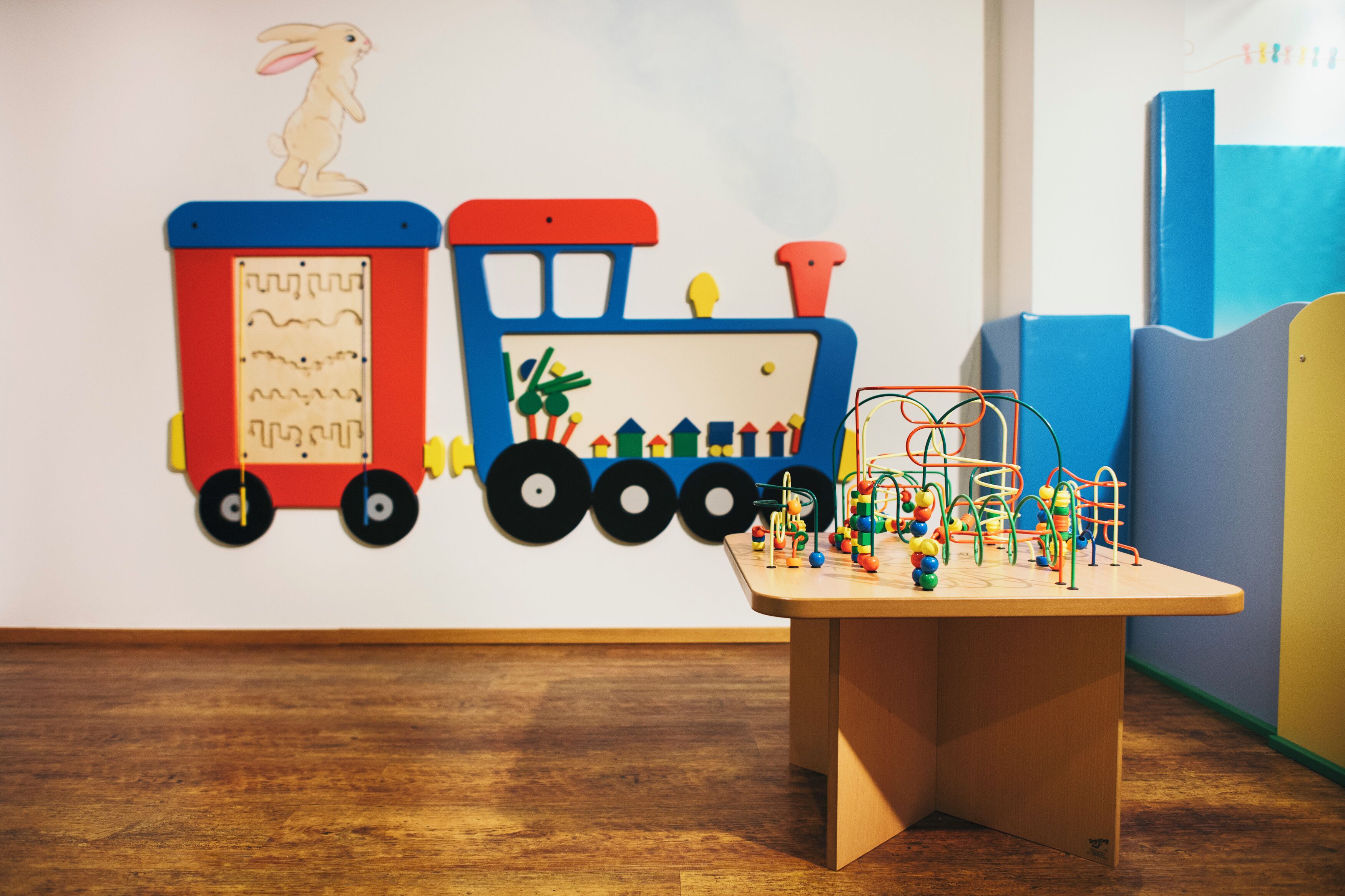 A room with a wooden floor, a table with toys, and a wall with a colorful mural.