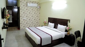 Habitación de hotel con una cama grande, una mesita de noche con lámpara, un escritorio pequeño con silla y un equipo de aire acondicionado en la pared.