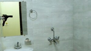 Un baño con lavamanos blanco, espejo, ducha y un cubo rosa.
