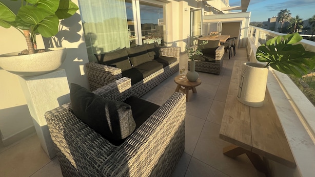 Un balcon agrémenté de meubles en osier, d’une plante en pot et d’une table sur laquelle est posé un vase.