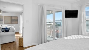 A bedroom with a large bed, a ceiling fan, a TV, and a balcony with curtains. - SurfsideVilla-3BR/2BA - Steps from the Sand! (Santa Rosa Beach)