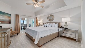 A spacious bedroom with a large bed, a ceiling fan, a bedside table with a lamp, and a view through a glass door. - Phoenix West, Lazy River, Beachfront, New Rental!! (Orange Beach)