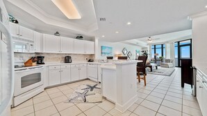 A modern kitchen with white cabinets, a central island, and a dining area with a view. - Phoenix West, Lazy River, Beachfront, New Rental!! (Orange Beach)