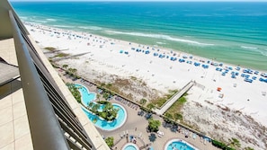 A beach resort with a pool area, beach umbrellas, and a view of the ocean.