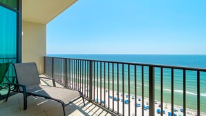 A balcony with a chair, overlooking a beach with umbrellas and the ocean. - Phoenix West, Lazy River, Beachfront, New Rental!! (Orange Beach)