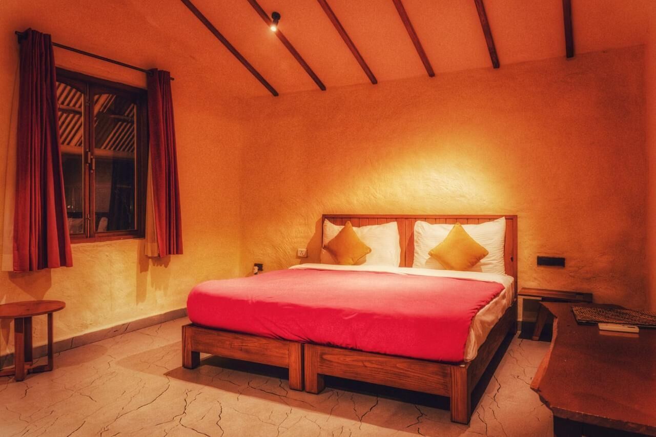 A bedroom with a wooden bed, red bedding, a nightstand, and a window with curtains.