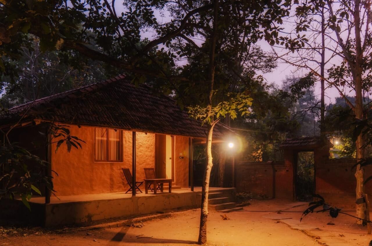 Una casa rústica con techo de paja, un porche con sillas y una entrada bien iluminada.