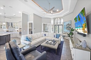 A modern living room with a sectional sofa, a coffee table, and a TV mounted on the wall. - Waterfront Home | W Exposure, Pool & Spa (Marco Island)
