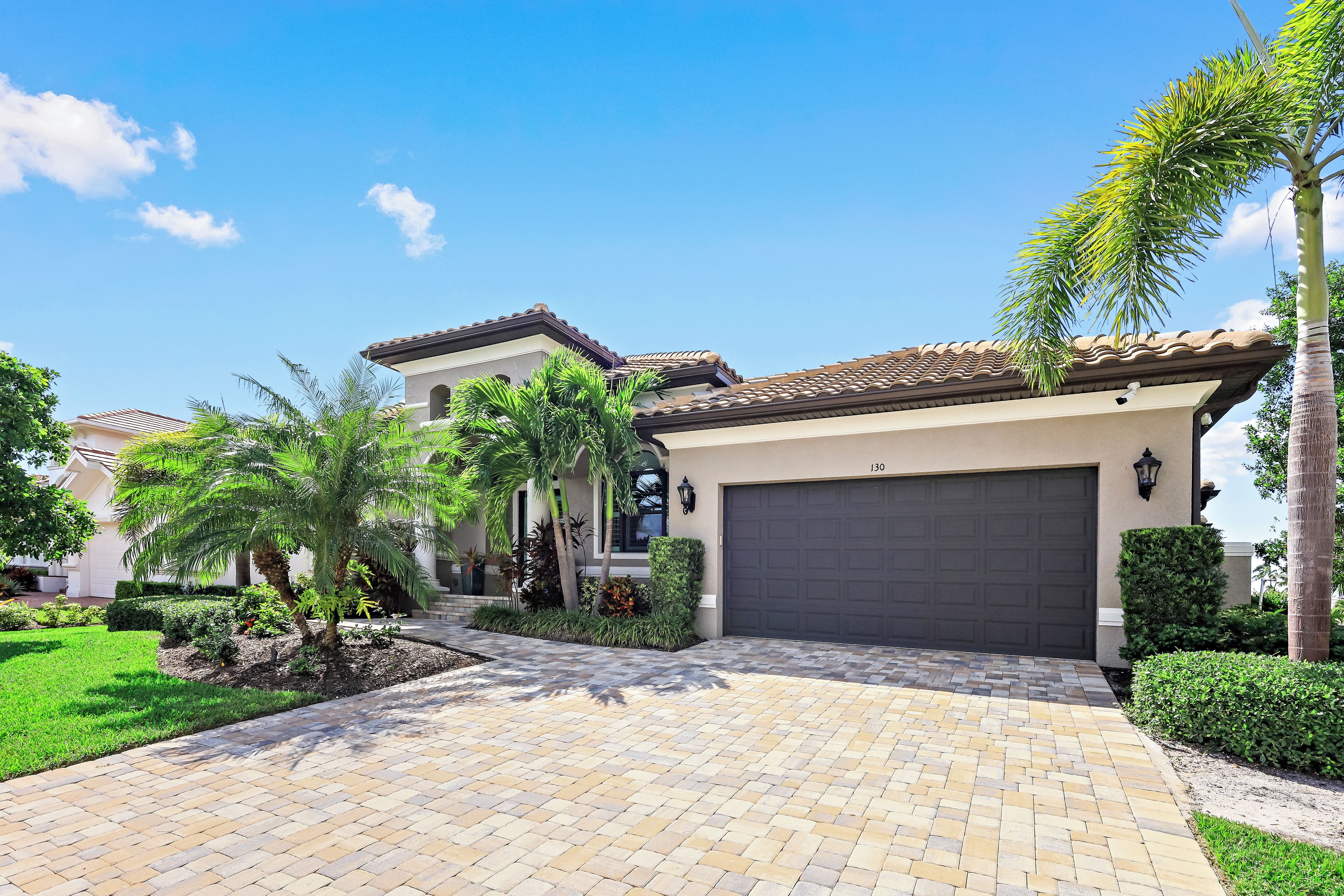 A residential property with a paved driveway, a garage, and a well-maintained garden with palm trees.