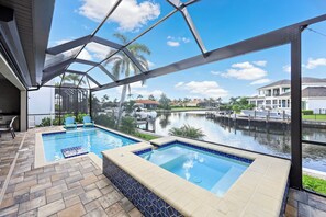 Área de piscina com duas banheiras de hidromassagem, um alpendre coberto e vista para um canal com barcos.
