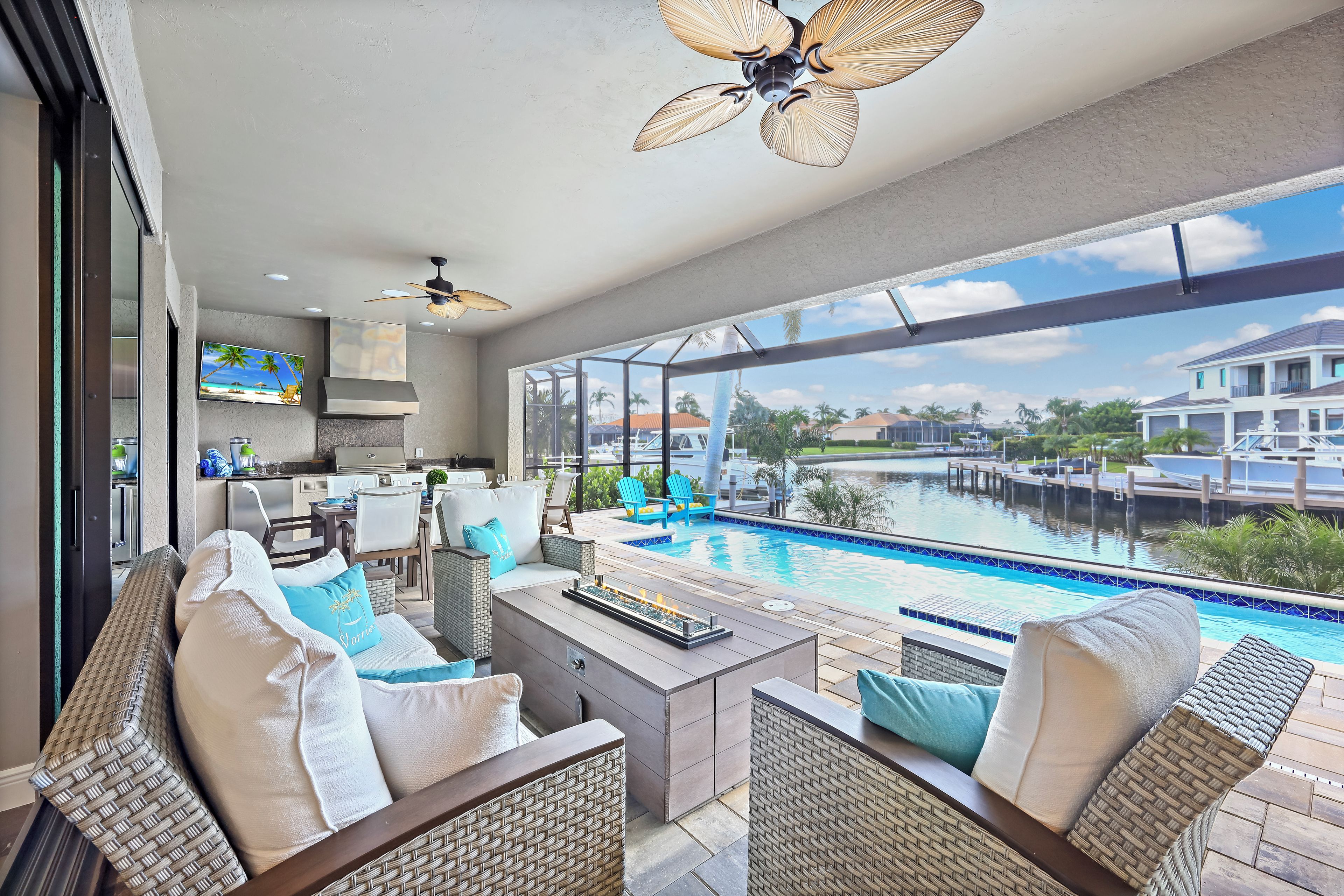 A poolside area with wicker furniture, a ceiling fan, and a view of a body of water and buildings.