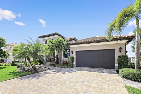 A residential property with a paved driveway, a garage, and a well-maintained garden with palm trees and shrubs. - Waterfront Home | W Exposure, Pool & Spa (Marco Island)