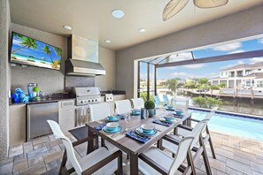 Cozinha moderna ao ar livre com área de refeições com vista para uma piscina.